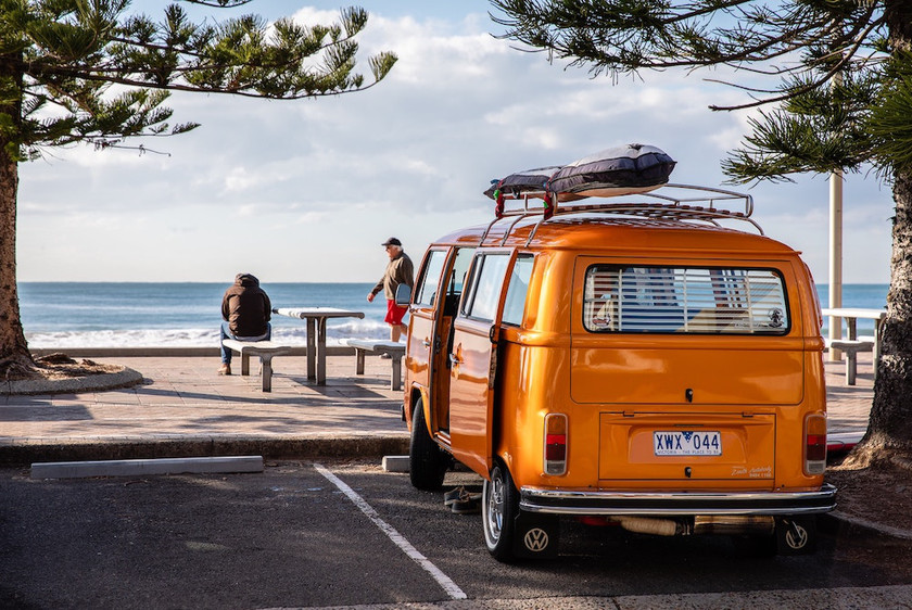 Campervan parkeret ved strand med surfboards på taget